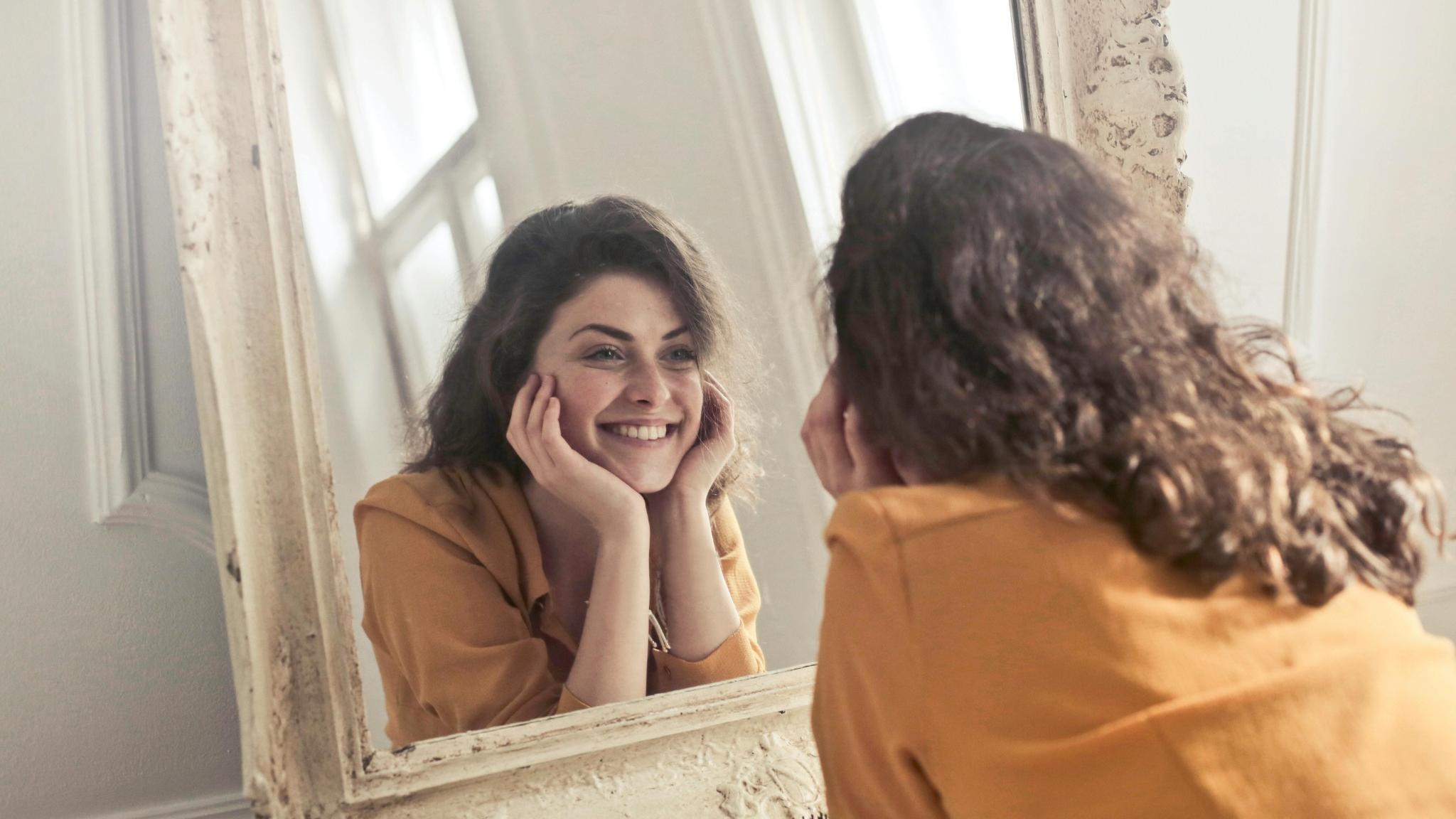 Donna che si guarda allo specchio con un sorriso autentico, simbolo di autostima, accettazione di sé e consapevolezza emotiva.