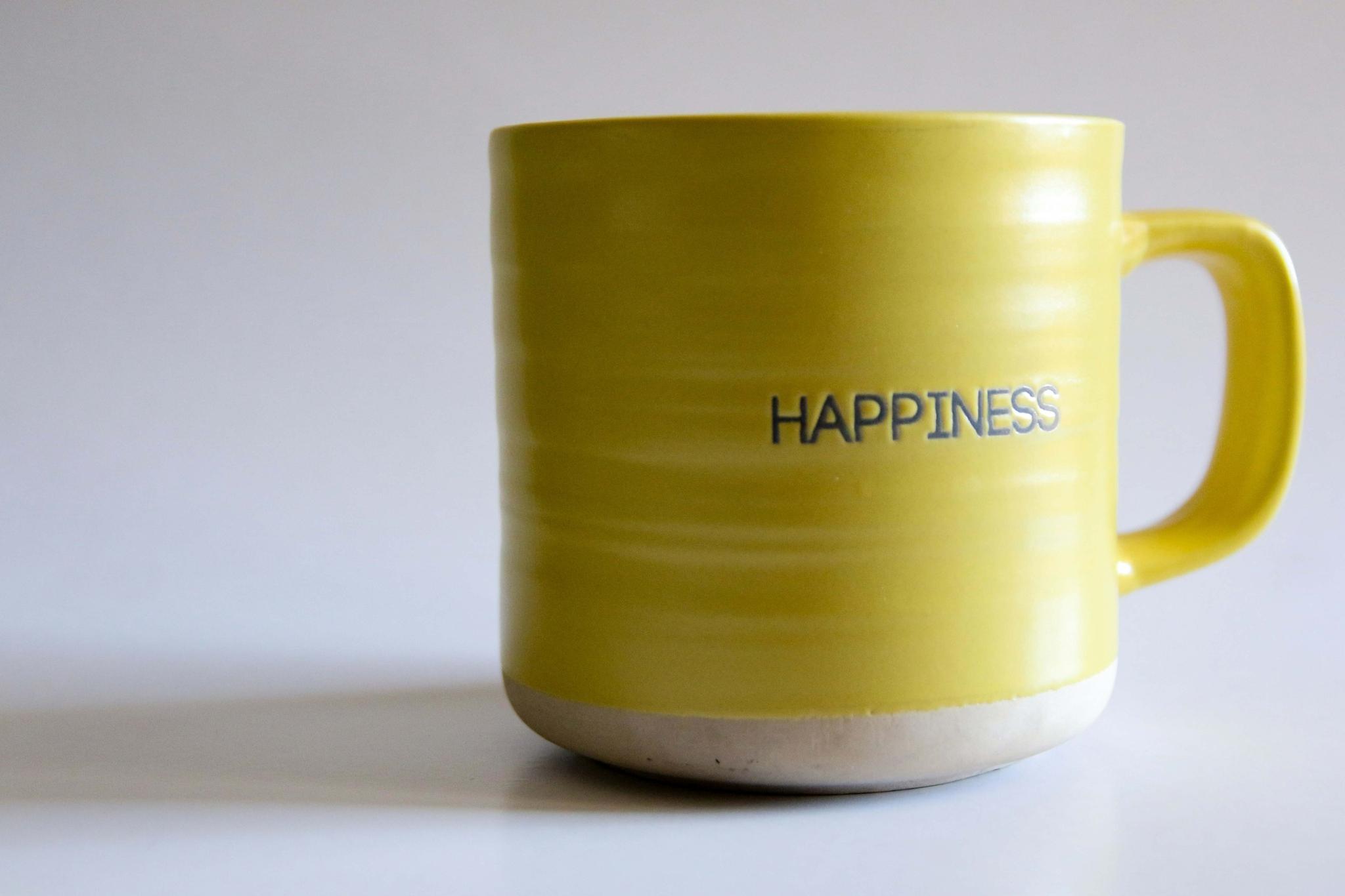 Contenuto articolo Tazza gialla con scritta ‘Happiness su sfondo neutro: simbolo del contrasto tra felicità superficiale e serenità interiore per il benessere psicologico.